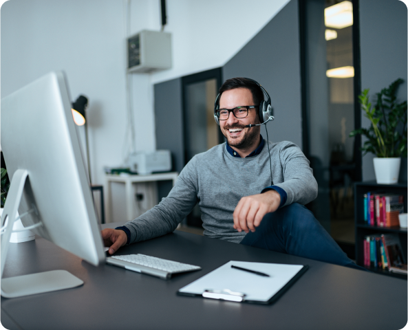 Homem com fones de ouvidos rindo em frente ao computador. Ele está em sua casa.